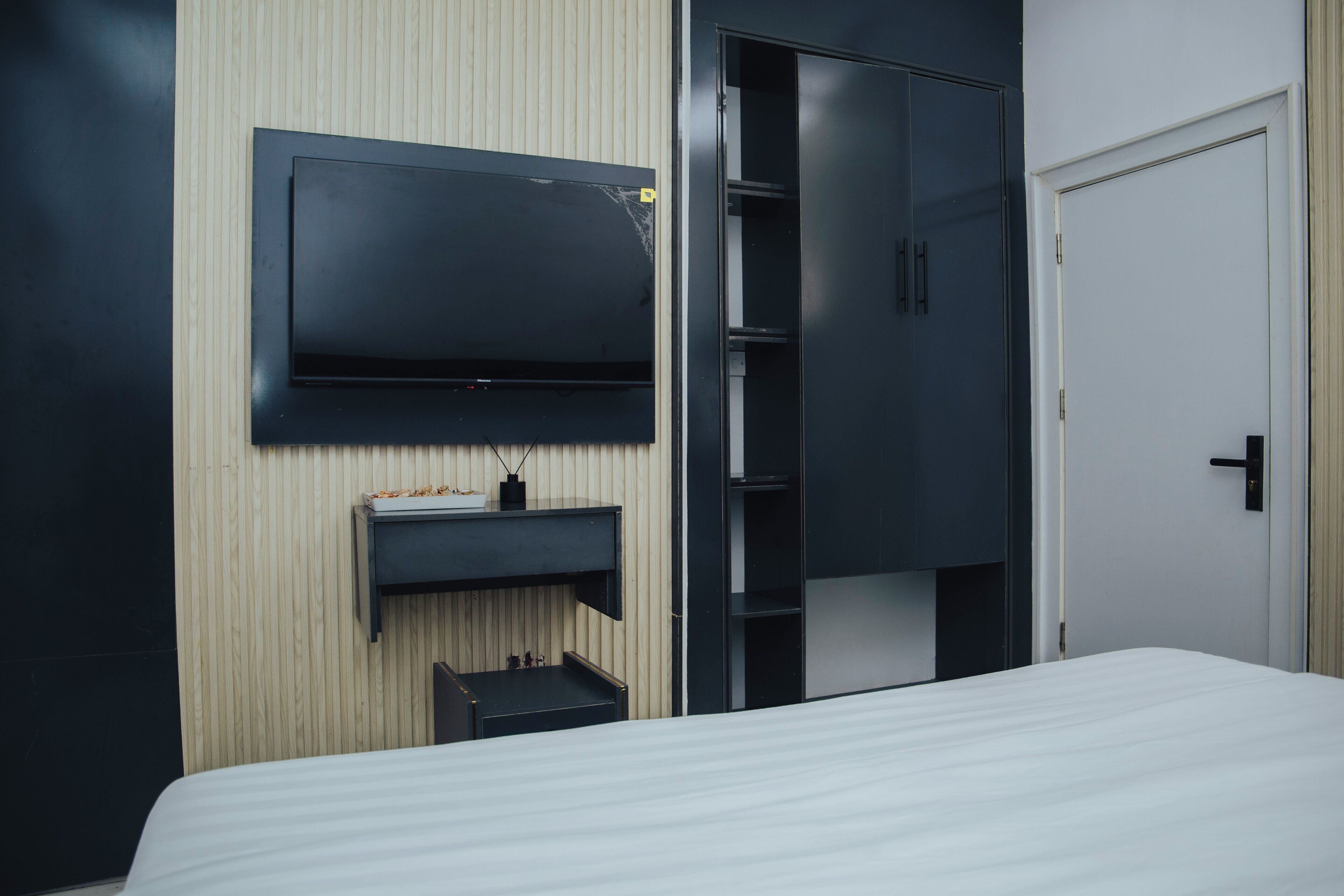 Ein Hotelzimmer mit Bett, Wandfernseher, Kleiderschrank und Tür.