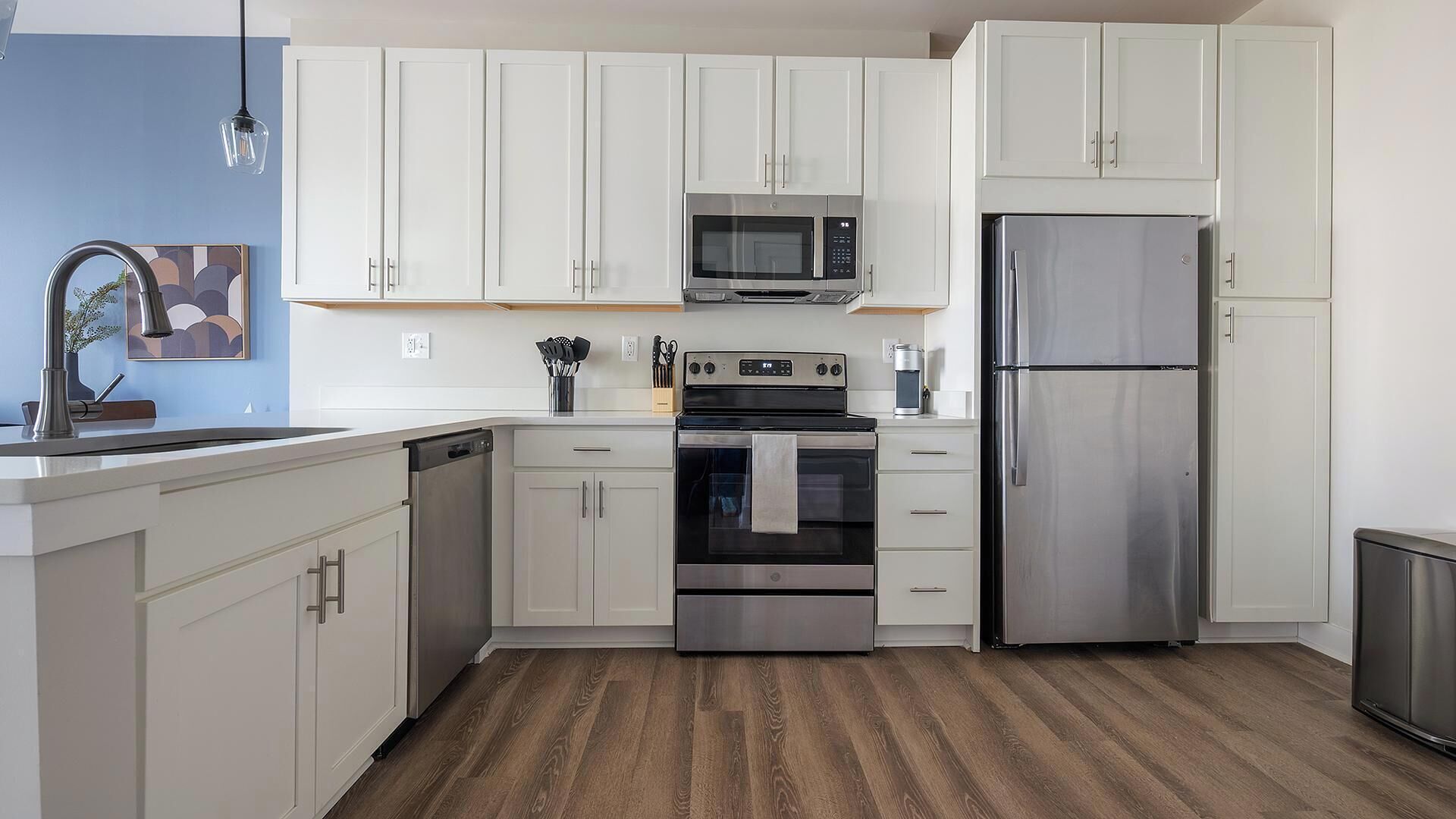 Een moderne keuken met witte kasten, roestvrijstalen apparatuur en een houten vloer.