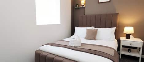 A hotel room with a bed, a nightstand, a lamp, and a framed picture on the wall.