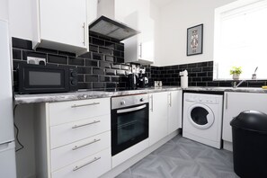A modern kitchen with a microwave, oven, and washing machine. - Modern 2-Bedroom Cardiff Apartment – Ideal for Families & Long Stays (Cardiff)