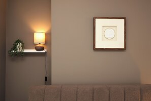 Eine Wandleuchte mit Pflanze, einem gerahmten Bild und einem Stromkabel an einer beige gestrichenen Wand.