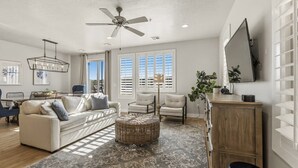A living room with a sofa, chairs, a ceiling fan, a TV, and a large window with blinds. - Private Balcony Hot Tub | Pool | Near Golf Course (Washington)