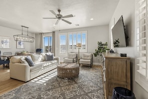 A living room with a sofa, chairs, a ceiling fan, a TV, and a large window with blinds. - Private Balcony Hot Tub | Pool | Near Golf Course (Washington)