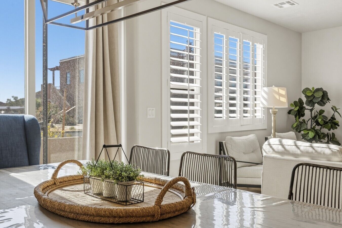 A modern living room with a glass table, wicker side table, and a view of the outside.
