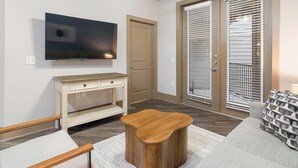 A modern living room with a flat-screen TV, a wooden coffee table, a sofa, and a patterned throw pillow. - Landing | Stylish 1BD, Clubhouse, Gym (Houston)