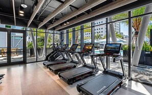 Ein Fitnessstudio mit Laufbändern, Ergometer und einem Pool, der durch große Fenster sichtbar ist.