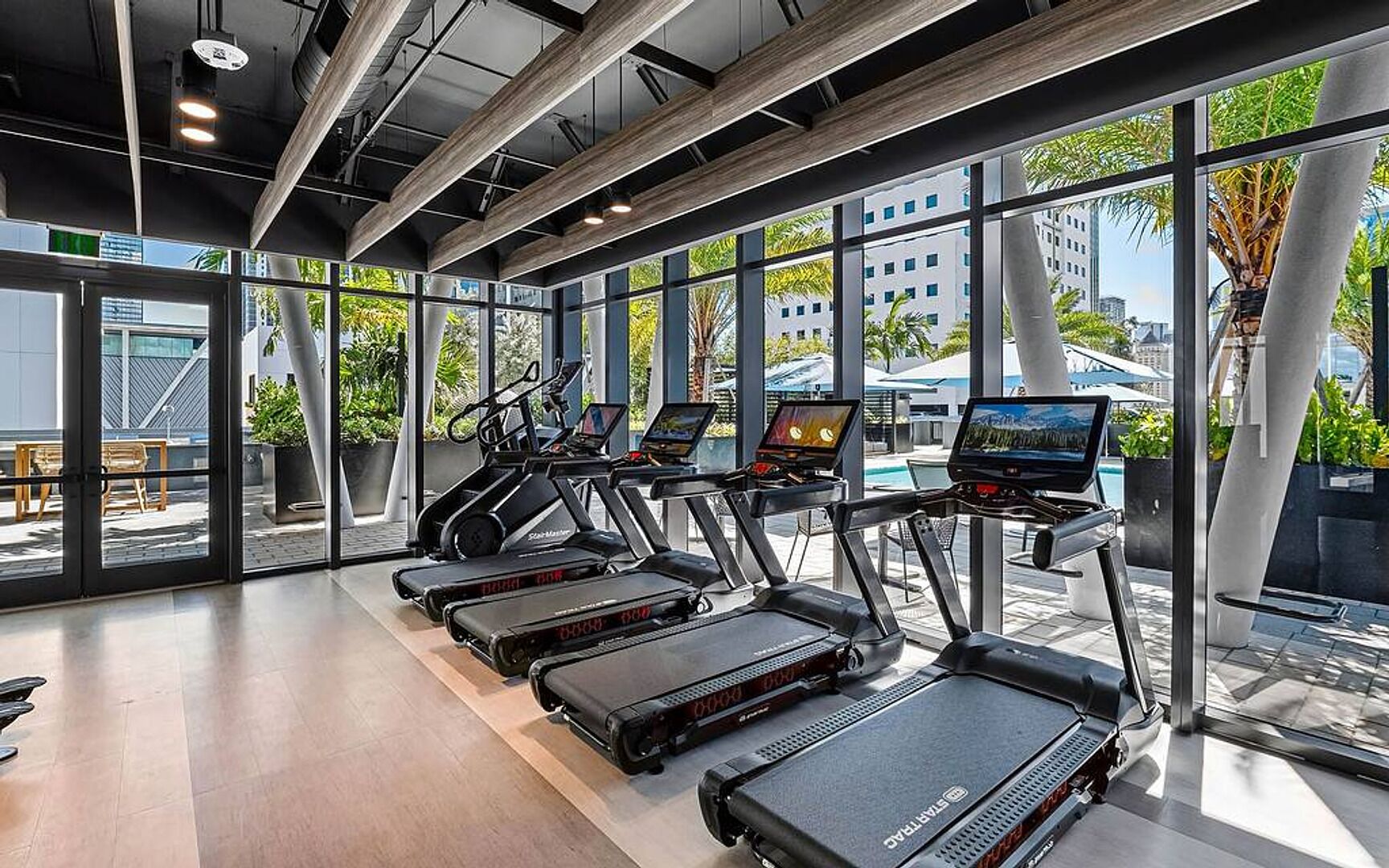 A gym with treadmills, exercise bikes, and a pool area visible through large windows.