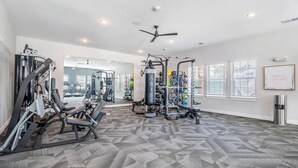A gym with various exercise equipment, a ceiling fan, and a view of the outside through large windows. - Landing | Modern 2BD in Shell Point (Port Royal)