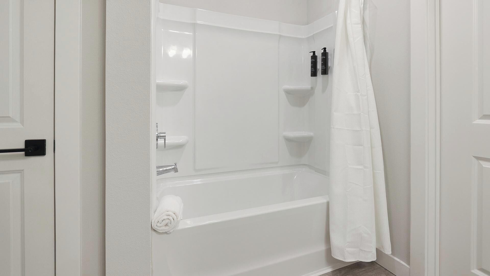 Une salle de bain blanche avec une baignoire, une serviette et deux bouteilles de shampoing.