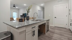 A modern kitchen with granite countertops, a built-in sink, and a dining area with a sofa and a coffee table. - Landing | Modern 2BD in Shell Point (Port Royal)