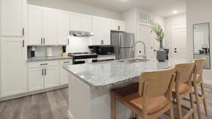 A modern kitchen with white cabinets, granite countertops, stainless steel appliances, and a central island with bar stools. - Landing | Modern 2BD in Shell Point (Port Royal)