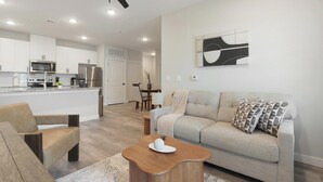A modern living room with a sofa, coffee table, and a dining area in the background. - Landing | Stylish 1BD in Shell Point (Port Royal)