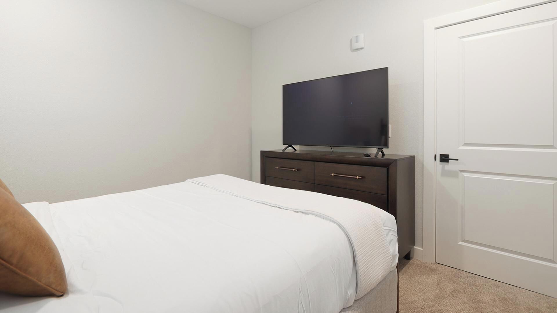 A bedroom with a bed, a dresser, a television, and a door.