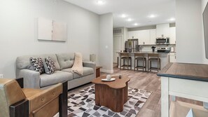 A modern living room with a sofa, coffee table, and a kitchen area with bar stools. - Landing | Stunning 2BD, Gym (Port Royal)