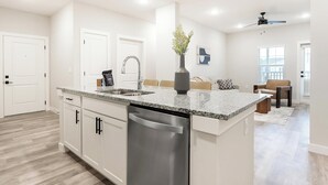 A modern kitchen with a dishwasher, double sink, and granite countertop. - Landing | Modern 2BD in Shell Point (Port Royal)