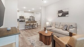 A modern living room with a sofa, coffee table, and a TV on a wooden stand. - Landing | Modern 2BD in Shell Point (Port Royal)