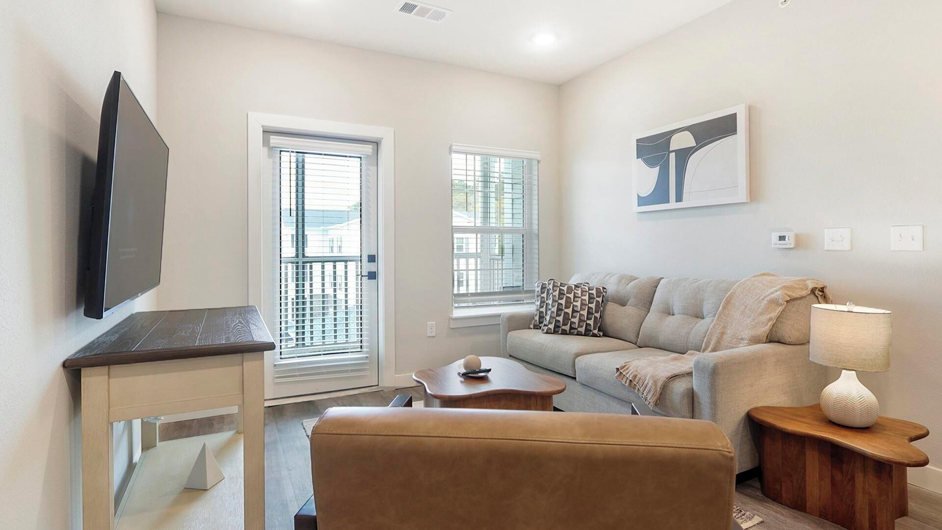 A living room with a sofa, a coffee table, a TV, and a door leading outside.