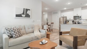 A modern living room with a sofa, armchair, and coffee table, a dining area with chairs, and a kitchen with white cabinets and appliances. - Landing | Stunning 1BD in Shell Point (Port Royal)