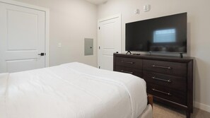 Une chambre à coucher avec un lit, une commode, un téléviseur et une porte.