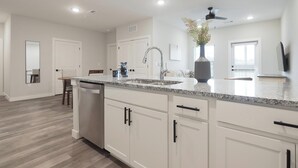 Une cuisine moderne avec des meubles blancs, des plans de travail en granit et un lave-vaisselle encastré.