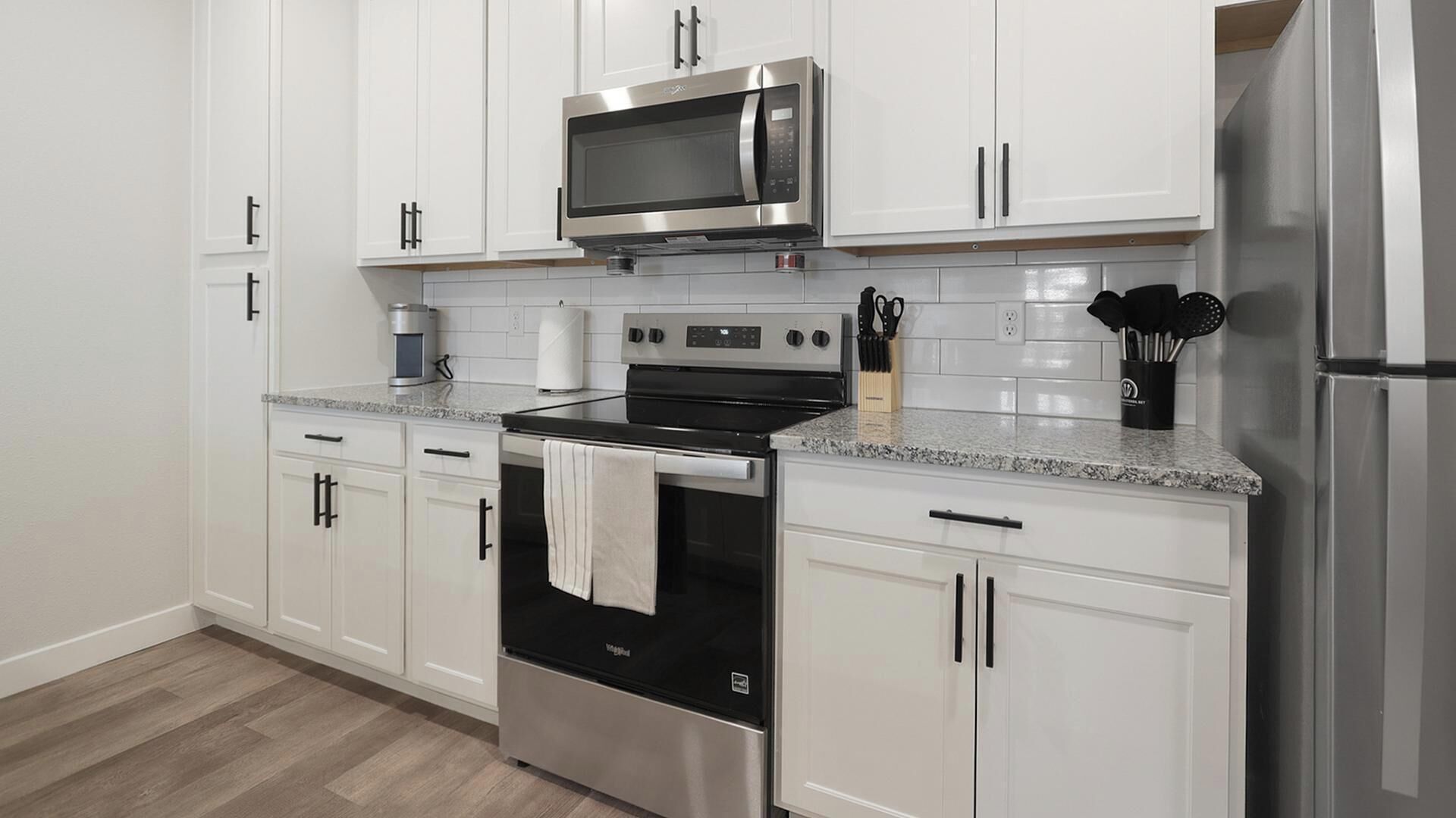 A modern kitchen with white cabinets, stainless steel appliances, and a granite countertop.