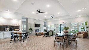 Un vaste espace de vie doté d’une cheminée, de ventilateurs de plafond et d’un coin repas avec une grande table et des chaises.
