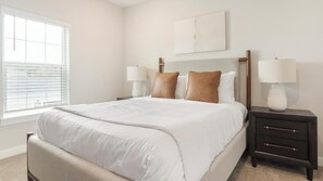 Een slaapkamer met een bed, nachtkastjes, een raam en een schilderij aan de muur.