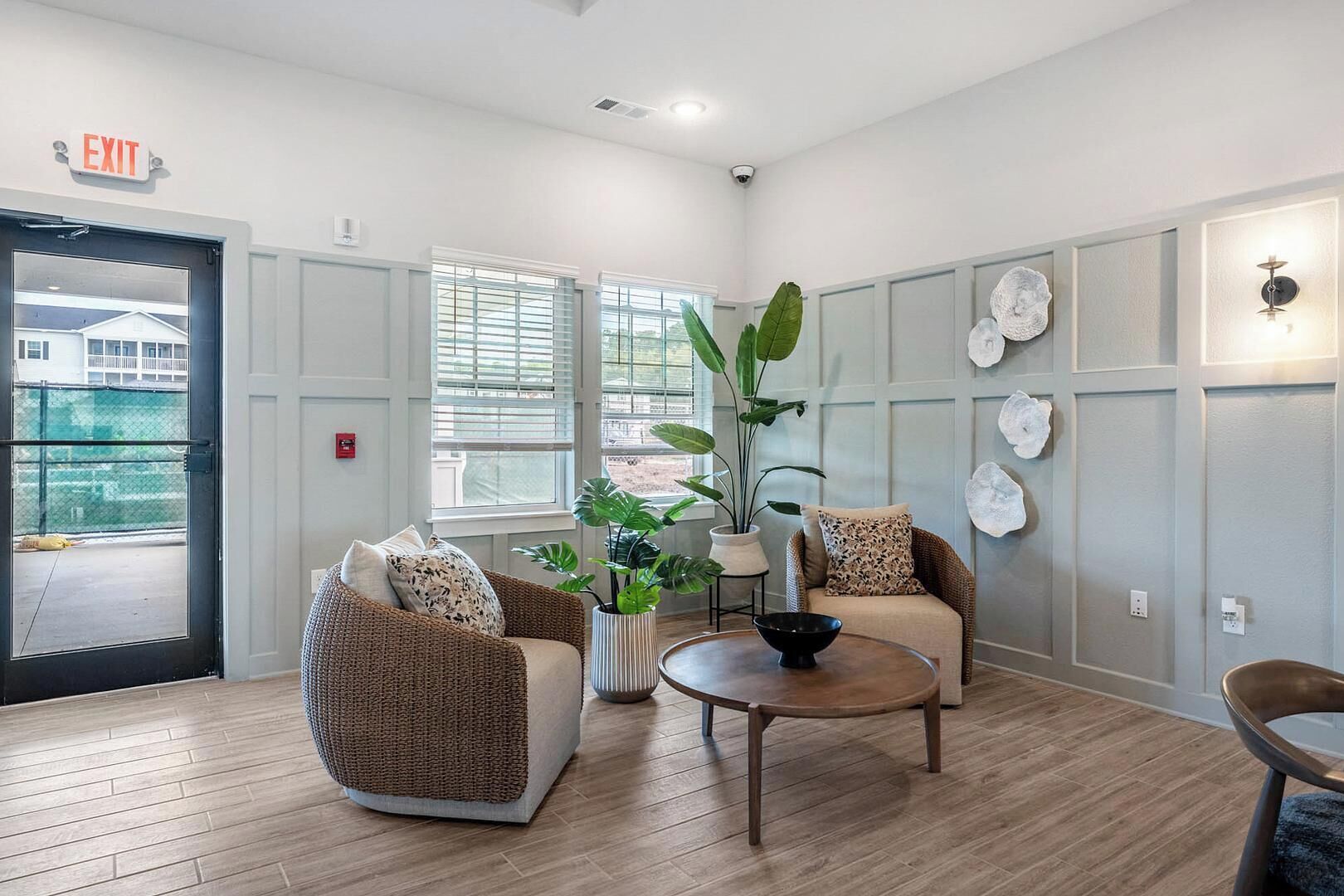 A room with wicker chairs, a round table, a potted plant, and wall-mounted decor.