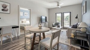 A modern living room with a round table, two sofas, a TV, and a balcony with sliding doors. - Landing | Chic 1BD in Medical Center (San Antonio)
