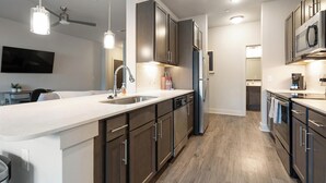 Une cuisine moderne dotée d’un îlot central, d’appareils électroménagers en acier inoxydable et de meubles de rangement en bois.