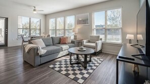 A modern living room with a grey sofa, a round coffee table, and a TV on a stand. - Landing | Stunning 2BD in Medical Center (San Antonio)