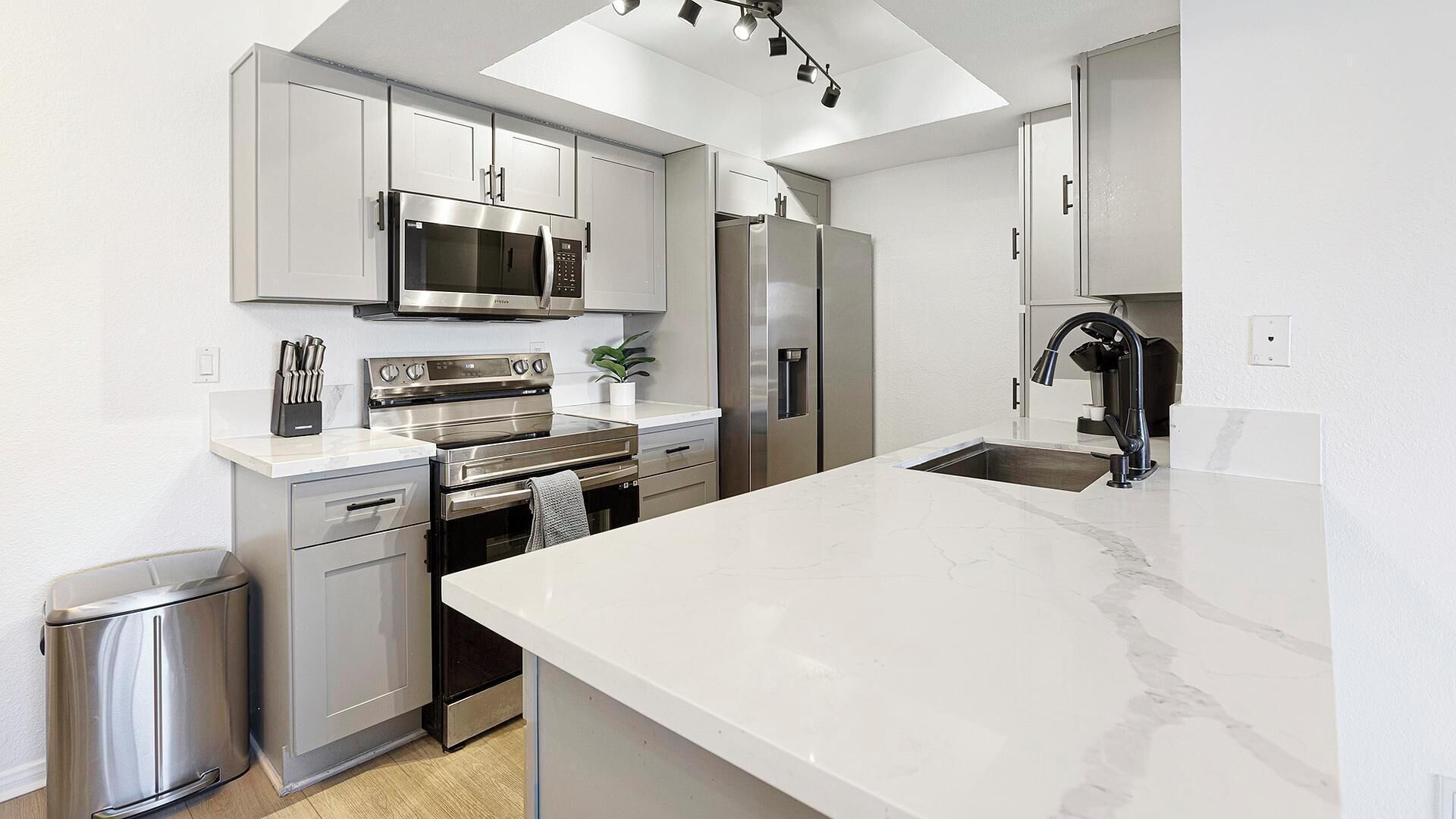 A modern kitchen with stainless steel appliances, a marble countertop, and a skylight.