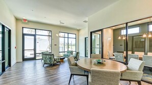 A conference room with a round table, several chairs, large windows, and an exit sign. - Landing | Modern 2BD, Clubhouse, Yoga Studio (Bonita Springs)