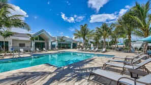A pool area with lounge chairs, palm trees, and modern buildings.