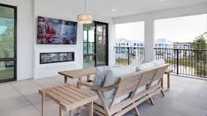 Un balcón moderno con una mesa y sofá de madera, ventanas amplias y un televisor montado.