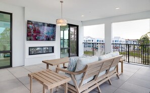 Ein moderner Balkon mit Holztisch und -sofa, großen Fenstern und einem an der Wand befestigten Fernseher.