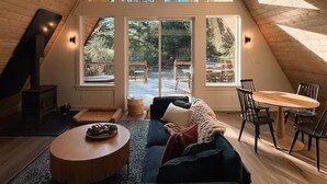 A spacious loft with a high ceiling, large windows, a chandelier, a cozy seating area, and a dining table. - NEW Mt Rainier Aframe | Sauna+Hot Tub | White Pass (Packwood)