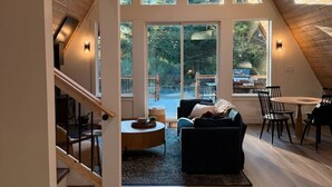 A spacious loft with a high ceiling, large windows, a cozy seating area, and a dining space. - NEW Mt Rainier Aframe | Sauna+Hot Tub | White Pass (Packwood)