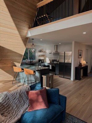 Et moderne køkken med en central ø, et spiseområde med barstole og et hyggeligt opholdsområde med en blå sofa.