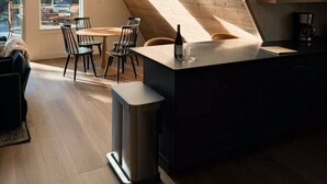 A modern kitchen with a sloped ceiling, large windows, and a dining area with chairs and a table. - NEW Mt Rainier Aframe | Sauna+Hot Tub | White Pass (Packwood)
