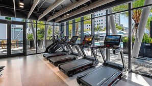 Ein Fitnessstudio mit Laufbändern, Ergometer und einem Pool, der durch große Fenster sichtbar ist.