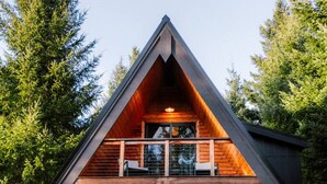 Una cabaña con techo triangular, fachada de madera y balcón con asientos.