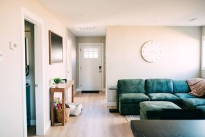Ein Wohnzimmer mit einem grünen Sofa, einer Wanduhr und einer Tür zu einem anderen Raum.