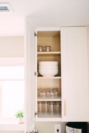 Eine Küche mit einem Schrank, der Glasbehälter, eine weiße Schüssel und eine Kaffeemaschine enthält.