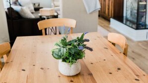 Uma mesa de jantar de madeira com uma planta em vaso no centro, rodeada por cadeiras.