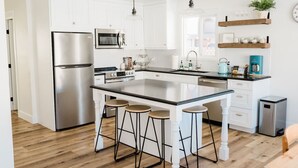 Uma cozinha moderna com armários brancos, eletrodomésticos de aço inoxidável, uma ilha grande com bancos e iluminação pendente.