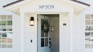 Um edifício branco com o número 'No 309' sobre a entrada, uma porta decorada com uma grinalda e um pequeno alpendre com degraus que levam até ele.