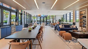 Une cuisine moderne avec une longue table à manger, des chaises et un coin salon donnant sur l’extérieur.