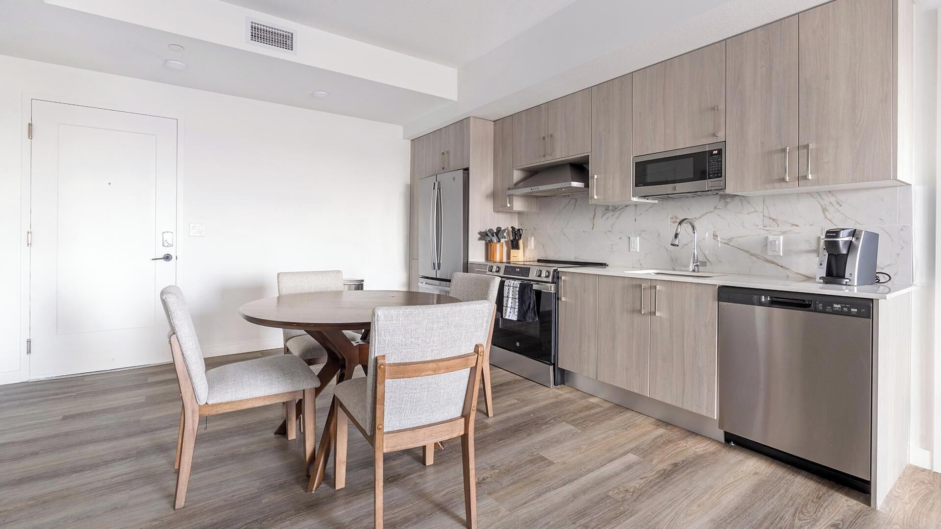 Una cocina moderna con comedor, electrodomésticos de acero inoxidable y muebles de madera clara.