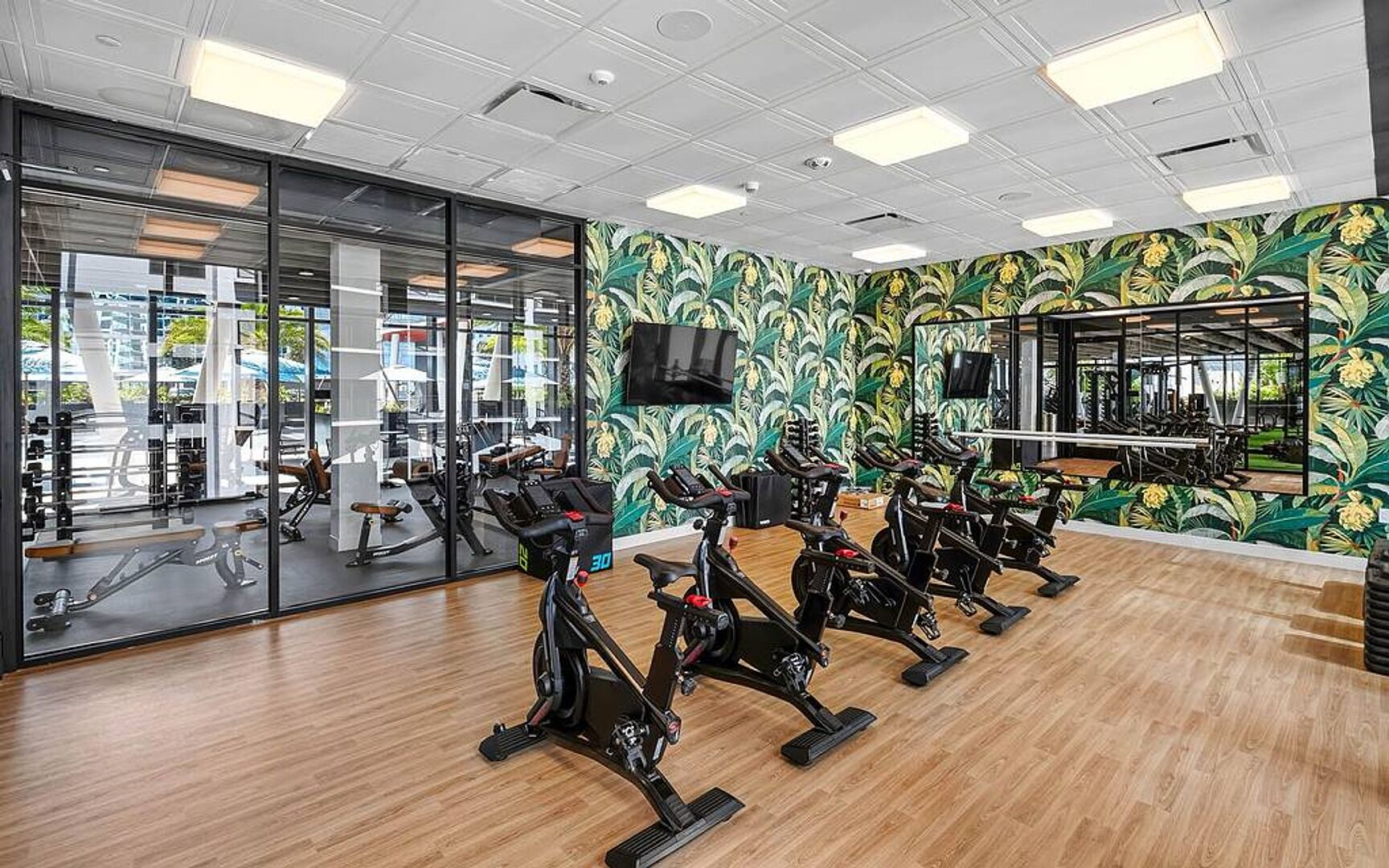 A gym with stationary bikes, a mirrored wall, and a view of outdoor exercise equipment.